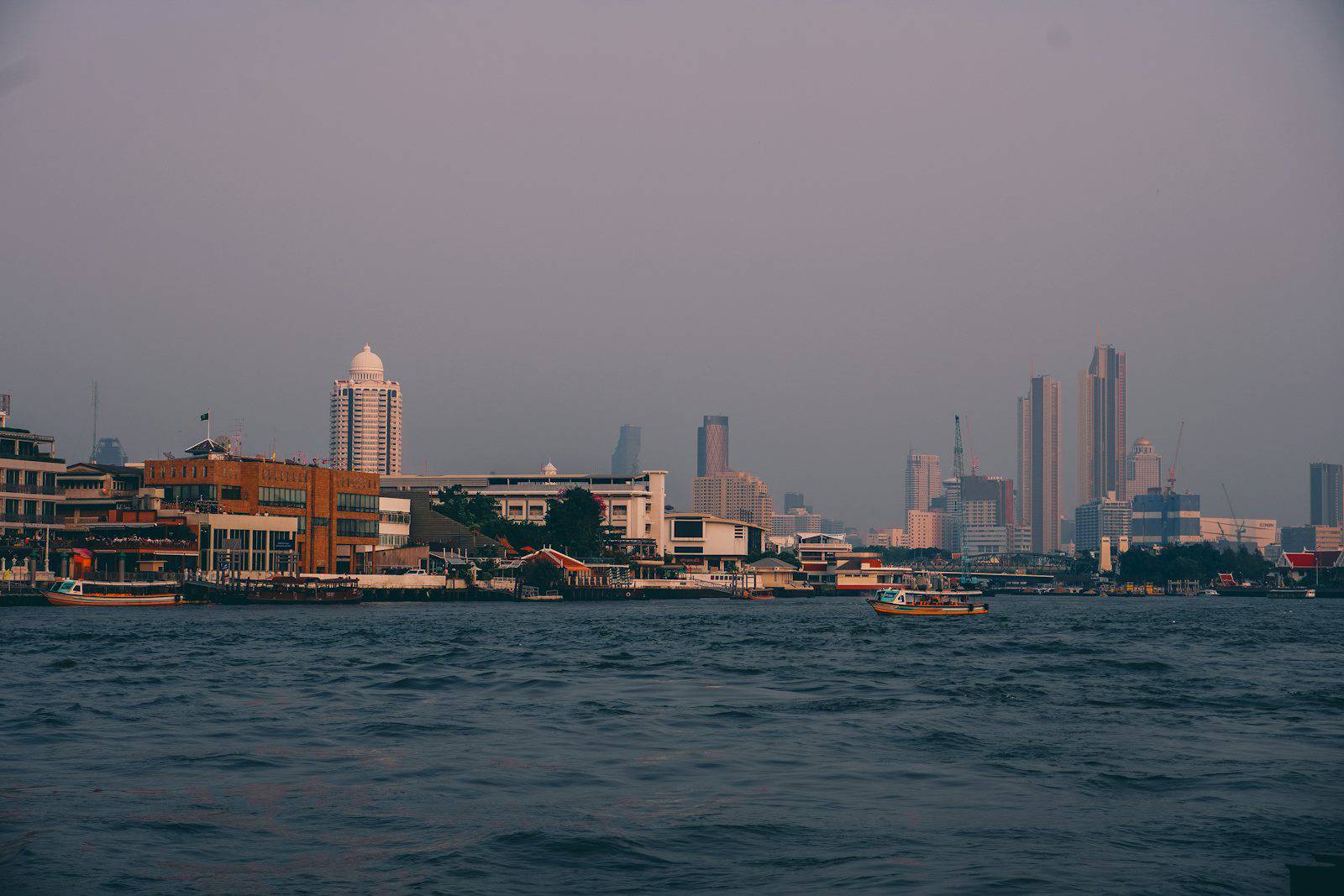 City skyline with boats on the water at dusk.