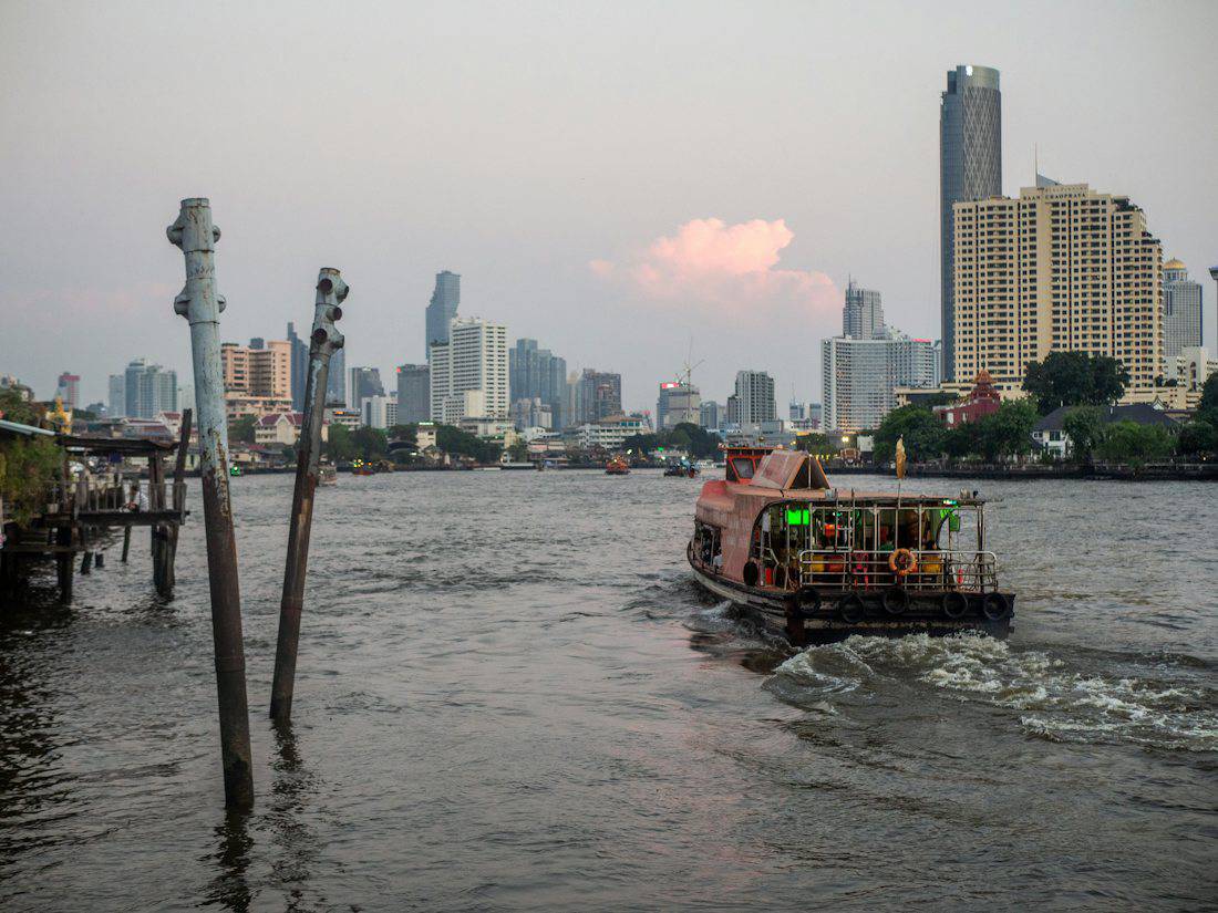 Ferry on the Chao Phraya River with Bangkok towers at dusk