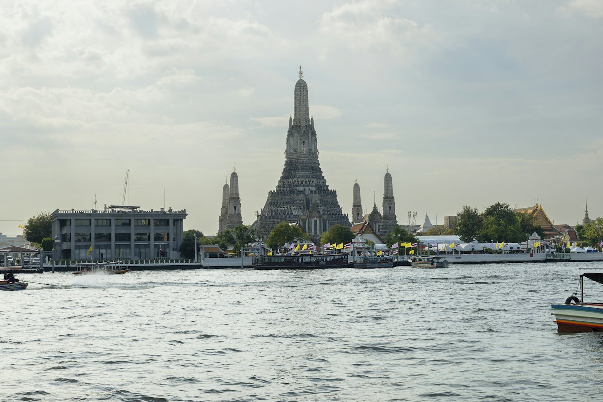 Wat Arun's central prang seen across the Chao Phraya, with boats passing on the river