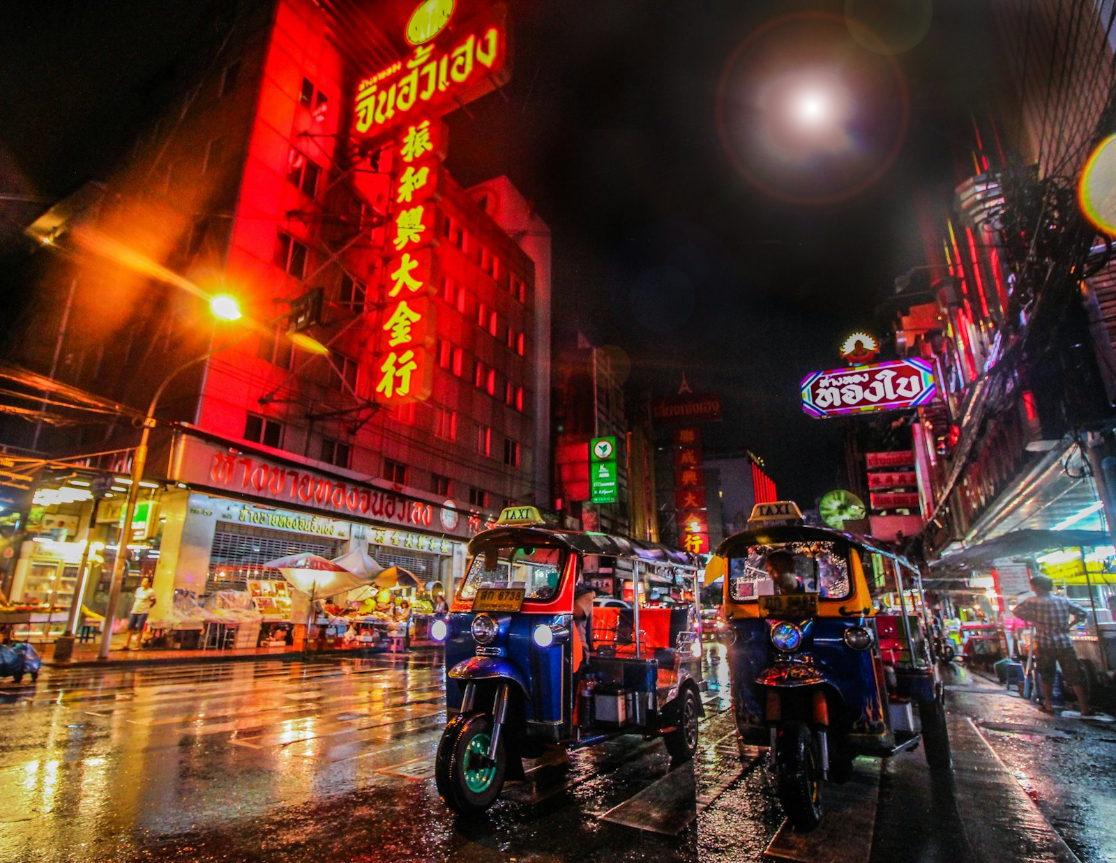 A neon-lit Bangkok street at night with tuk-tuks parked along it