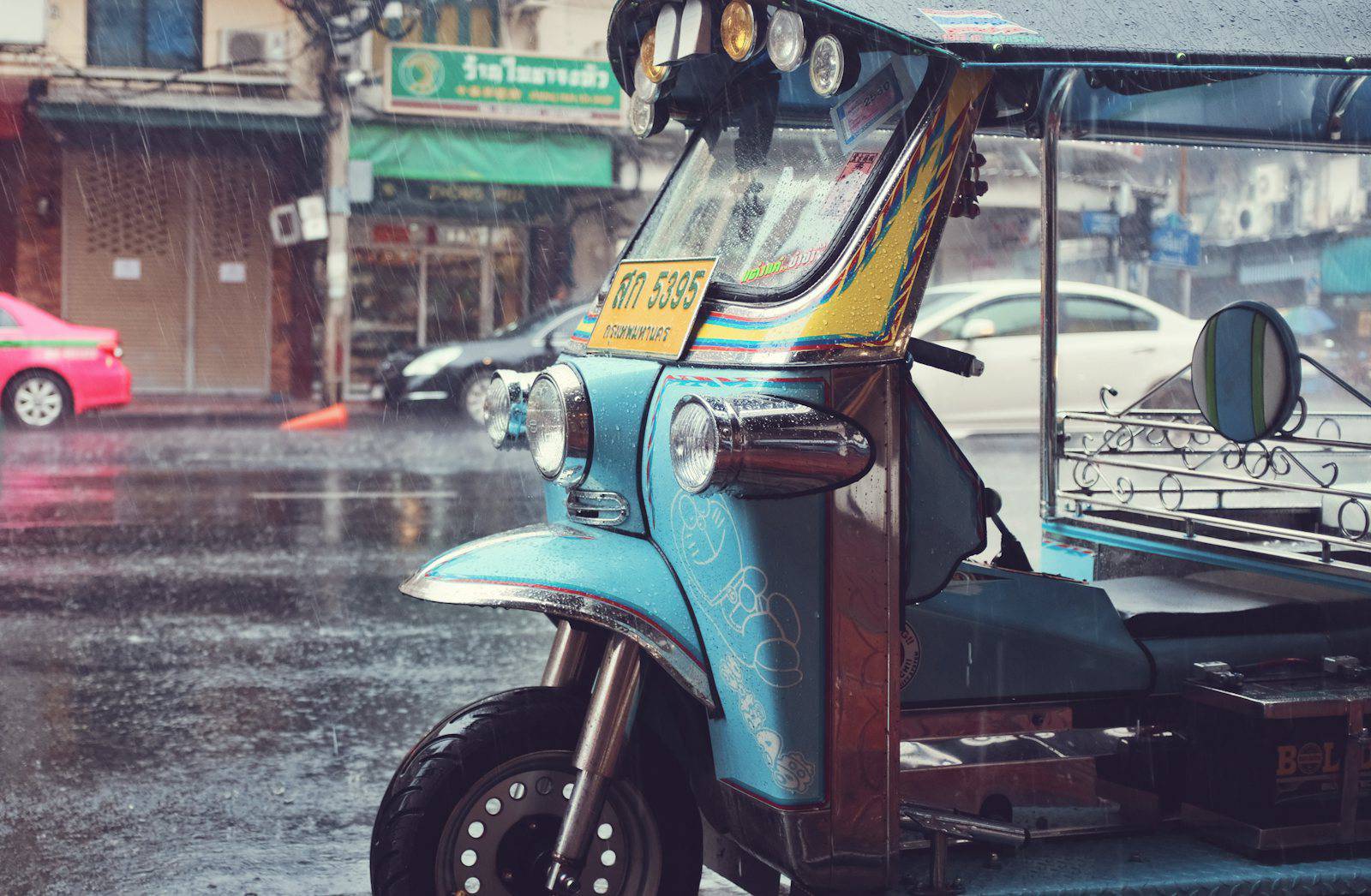 Tuk tuk parked on a wet Bangkok street during heavy rain