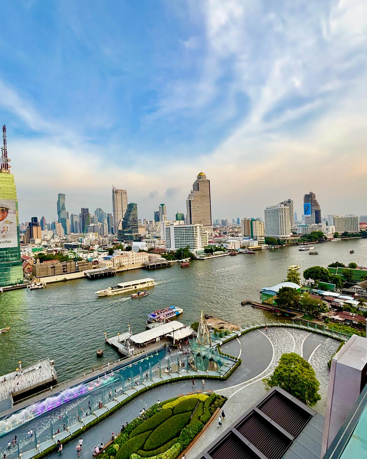 The Chao Phraya River from ICONSIAM, with express boats on the water, piers on both banks and the Silom and Sathorn skyline behind